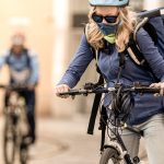 Photo of bike courier with long light coloured hair in urban centre wearing a face mask.