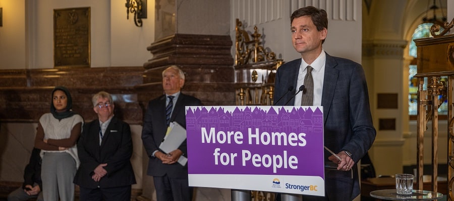 David Eby at a press conference standing in front of a podium labeled "More Homes for People"